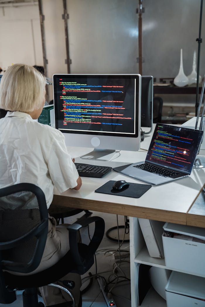 Woman programmer coding on dual monitors in a modern office setting, focusing on software development.