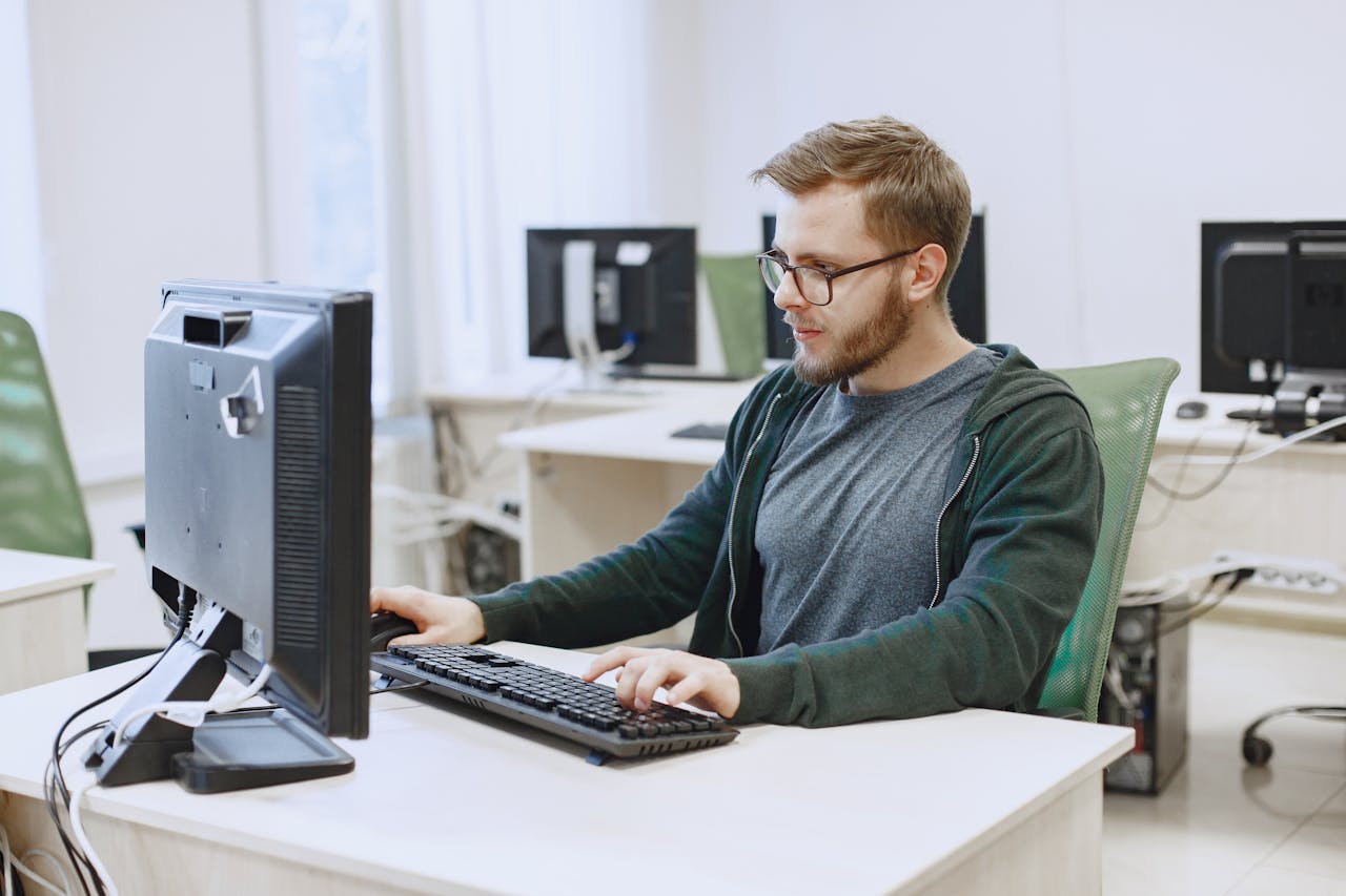 Young man with eyeglasses working on a desktop computer in a modern office environment.
