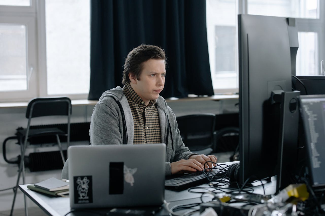 A dedicated programmer focused on coding at his workspace with dual monitors in a modern office setting.