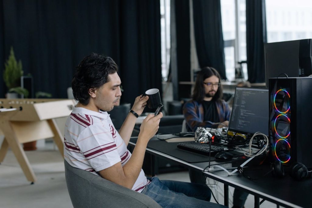 Two programmers at work in a modern office, focused on coding and enjoying a coffee break.